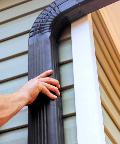 On roof, worker is installing rain gutter fitting downpipe downspout bend